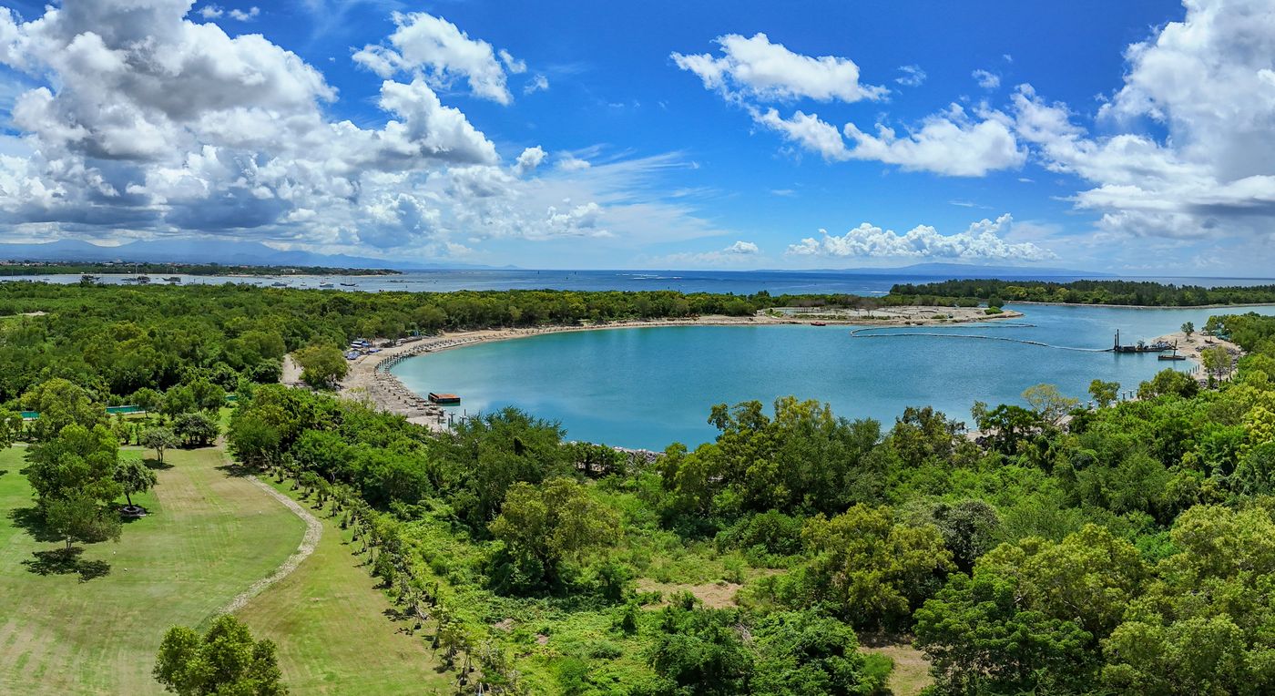 Aerial view of a sheltered turquoise bay on the south Bali coast, fringed by beach and trees